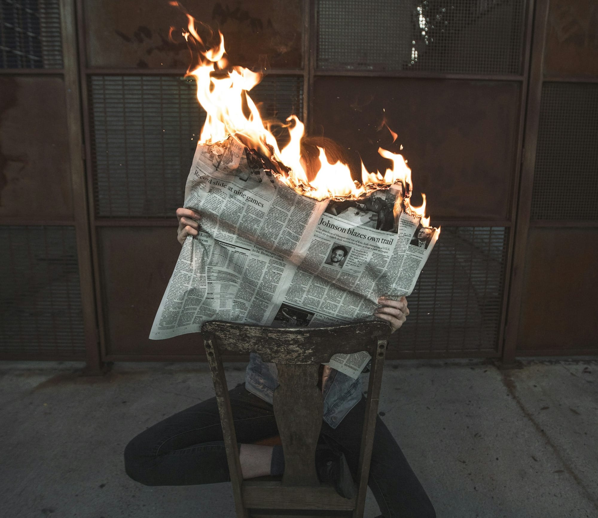 woman reading a newspaper that's on fire while sitting on an old wooden chair