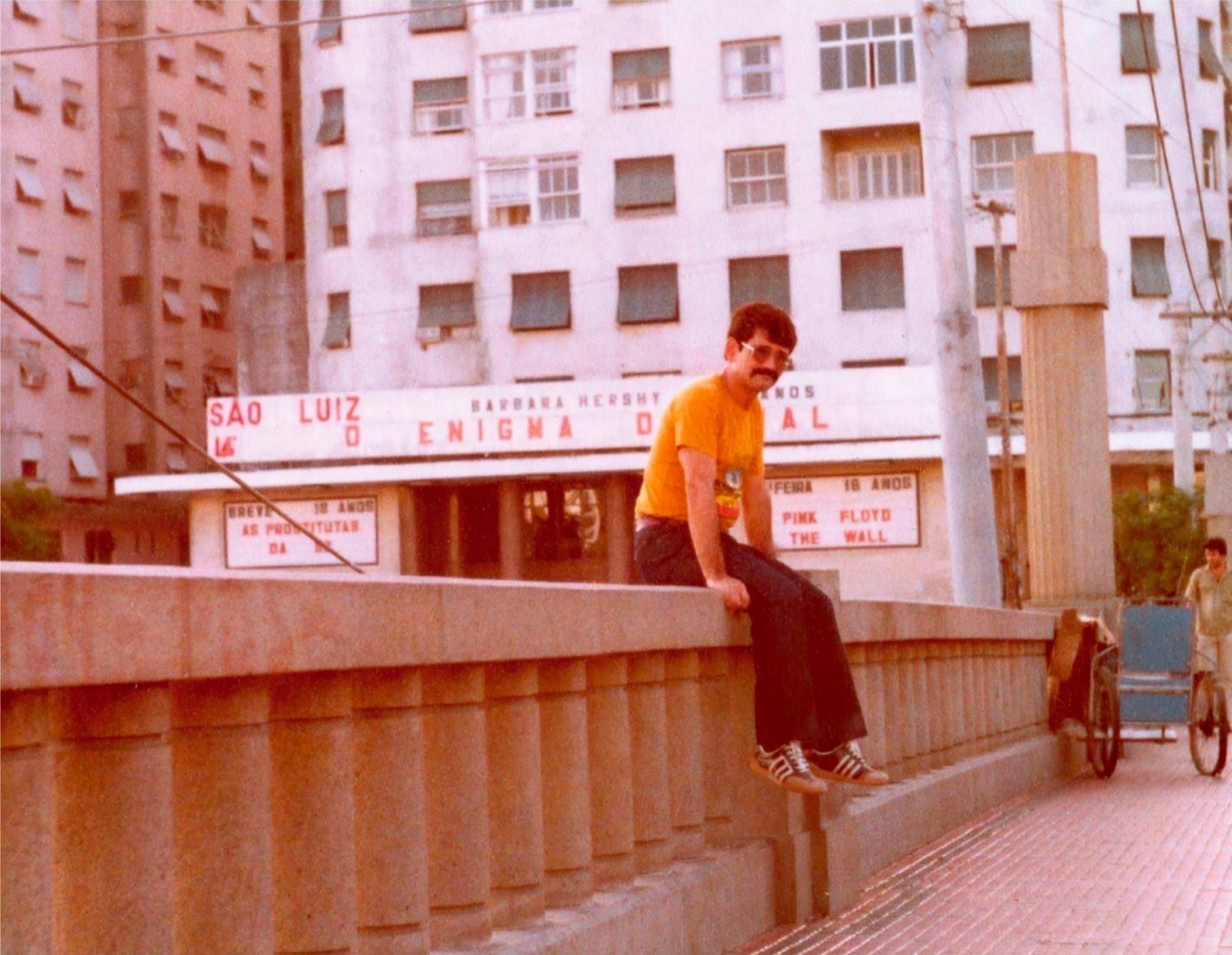 photo of a man in sunglasses sitting on a bridge in front of a movie theater